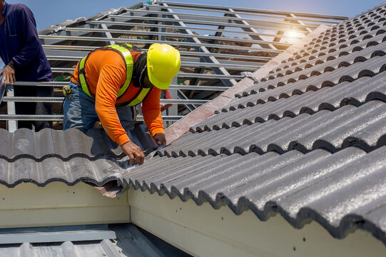 Roof repair,  construction worker repairing roof,replacing gray tiles or shingles on house with blue sky as background and copy space, Roofing - construction worker standing on a roof covering it with
