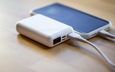 A smartphone is charged from a small white power bank.