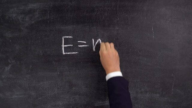 The teacher's hand writes the formula E=mc2 on the blackboard