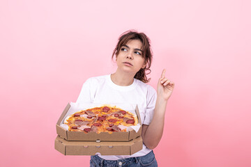 Pensive attractive girl with pizza in a box on a pink background, copy space.