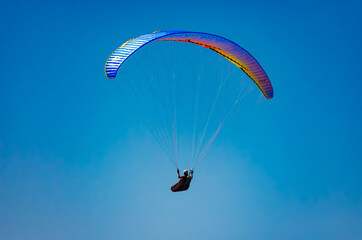 Paraglider gliding away in the blue sky. 