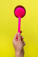 Female hand holding house cleaning scrubbing brush tool on yellow background.