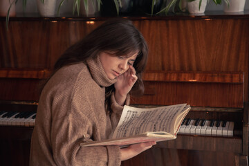 Young woman musician looks into a collection of notes, sitting at the piano.