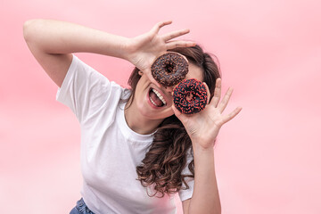 Pretty smiling woman holding donuts in her hands on a pink background.