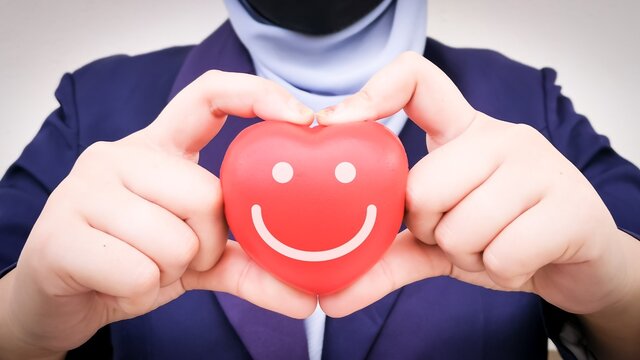 Red heart shape with smiling face hold by business woman.