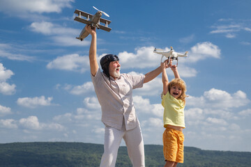 Grandfather and son with plane and quadcopter drone over blue sky and clouds background. Elderly old relative with child.