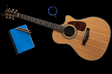 Classical acoustic guitar, notepad and a cup of coffee on a black background.