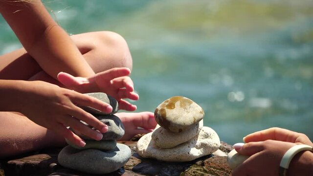Woman bilds stones pyramid on the seashore on a sunny day on the blue sea background. Happy holidays. Pebble beach, calm sea, travel destination. Concept of happy vacation on the sea, meditation, spa