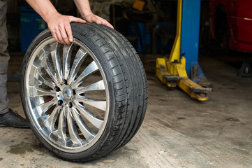 Obraz na płótnie Canvas An auto mechanic holds a wheel of a car. Change of car tires according to the season