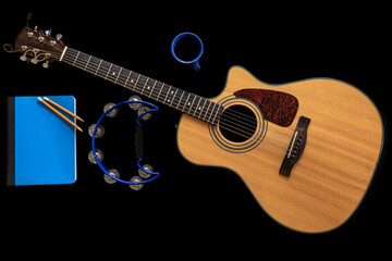 Acoustic guitar, notepad, tambourine and a cup of coffee on a black background.