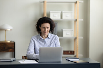Concentrated middle aged business woman looking at computer screen, working distantly on online project at modern home office, enjoying studying on internet courses or communicating distantly.