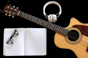 Obraz na płótnie Canvas Classical acoustic guitar, headphones and notebook on a black background.