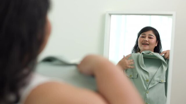 Body positive plus size female clothing. Body positive plus size woman happily and is proud of herself looking at mirror at home 