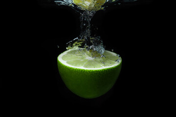 Fototapeta na wymiar A slice of lime falls into the water on a black background. Sour fruit. Citrus fruit