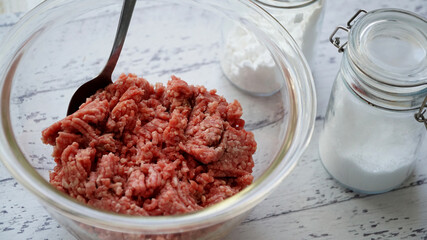 ガラス製のボールに入った生の合い挽きに肉とスプーン、調味料
