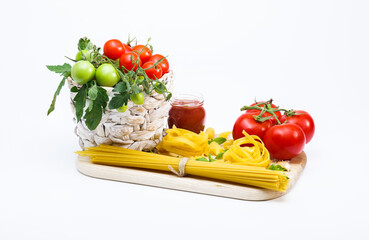 Tomatoes in a wicker basket, spaghetti, tagliatelle, chilli tomato sauce, red ketchup, and fresh ingredients: cherry tomatoes, garlic, basil on a wooden board
