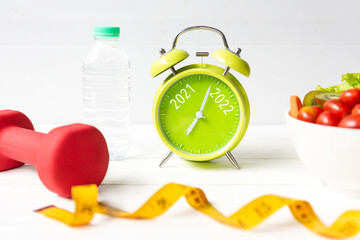 2021 and 2022 on alarm clock with workout planing for dieting. Sport exercise equipment workout and gym nutrition fresh salad for fitness. Merry Christmas and Happy new year concept