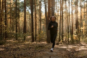 Young athletic woman jogging in forest in sunny morning. Healthy lifestyle concept.