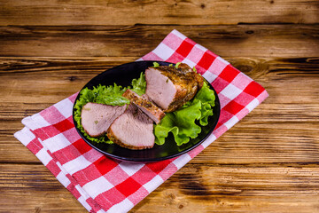 Slices of baked pork meat and lettuce leaves on a black plate