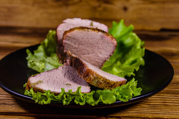 Slices of baked pork meat and lettuce leaves on a black plate