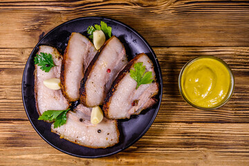 Slices of baked pork belly, garlic and parsley on a black plate. Top view