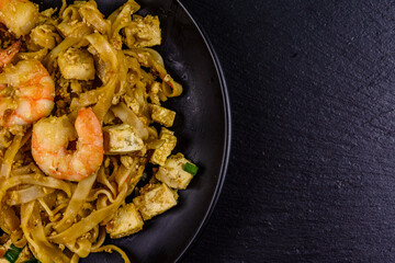 Black plate with pad thai on a slate board. Top view