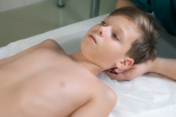 Session of craniosacral therapy, cure of teen boy's back of the head and neck by a doctor therapist. Craniosacral therapist touches boy's head and corrects spine at hospital. Boy is lying on couch.