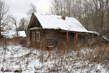 An old dilapidated wooden farmhouse in winter landscape. An abandoned village and the first snow