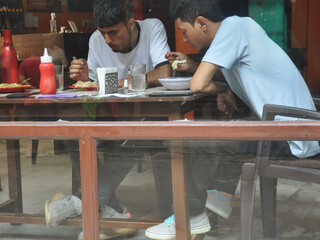 View of people eating food in the cafe seen through the window glass.