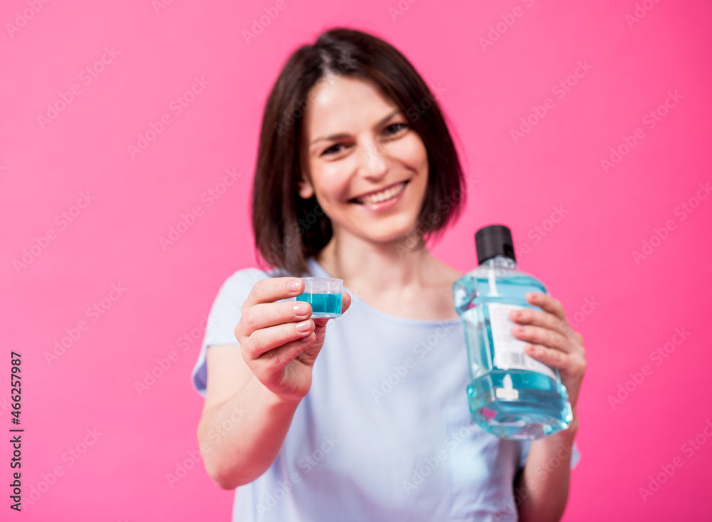 Wall mural beautiful girl uses mouthwash on the pink background