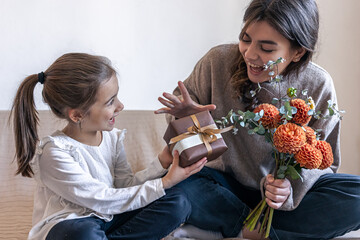 A little girl gives her mother a gift and a bouquet of flowers.