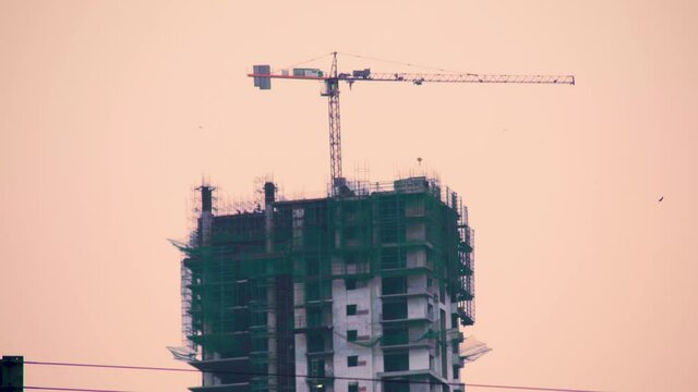 zoomed shot of an under construction building with green safety nets and a crane on top of the half finished skyscraper multi story building showing the rapid expansion of real estate in noida
