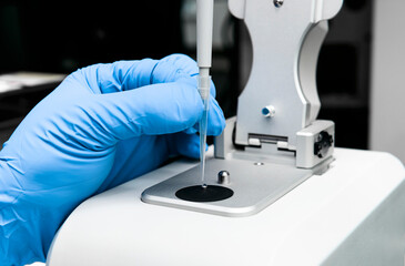 Scientist holds micropipette and loads sample onto low pedestal of Nanodrop for measuring the...