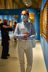 Woman visitor wearing an antivirus mask in the historical museum looking at pictures.
