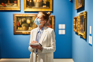 Woman visitor wearing an antivirus mask in the historical museum looking at pictures.