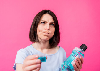 Beautiful girl uses mouthwash on the pink background