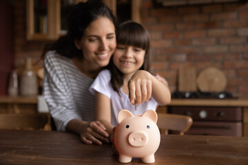 Happy mom teaching smart daughter girl to save invest money, motivate child for accounting, investment, planning future. Kid dropping cash into pink piggy bank. Family economy. Close up