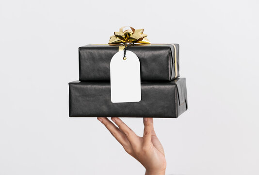 Hand holding black gift box and mockup christmas greeting tags on white background.