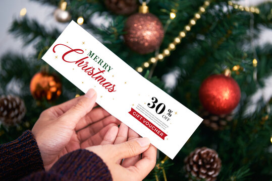 Hand holding christmas gift voucher tags label on christmas tree background.