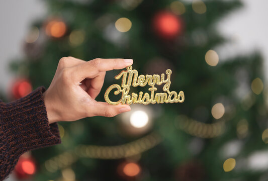 Woman hand holding merry christmas text for decorating a Christmas tree in christmas day.