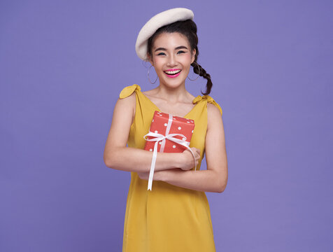 Young asian woman happy holding gift box on bright purple background. merry christmas and new year.