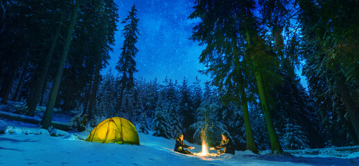 couple camping with campfire and tent outdoors in winter forest