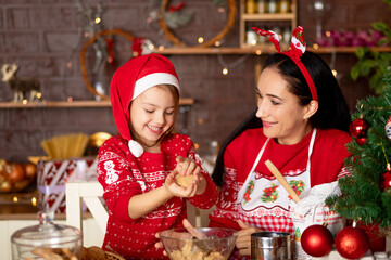 mom and daughter in a dark kitchen with a Christmas tree cook ginger cookies for the New Year or Christmas and smile in a Santa Claus hat