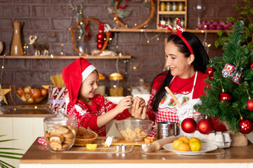 mom and daughter in a dark kitchen with a Christmas tree cook ginger cookies for the New Year or Christmas and smile in a Santa Claus hat