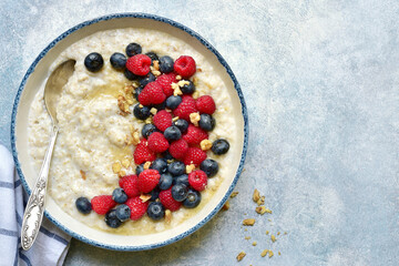 Oatmeal porridge with fresh berries and honey for a breakfast, Top view with copy space.
