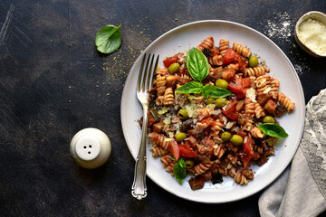 Fusilli pasta with tomatoes, eggplants and olives. Top view with copy space.