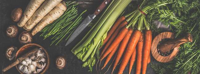 Various vegetables and kitchen utensils on dark rustic kitchen table: Carrots, garlic, mushrooms, celery and parsnip. Healthy lifestyle with vegetarian food. Top view. Banner. - obrazy, fototapety, plakaty