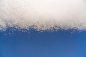 Fluffy clouds in the blue sky, they are arranged in a flat strip.