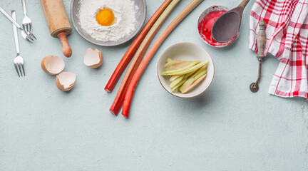 Baking preparation with rhubarb, egg yolk, flour, egg shell, wooden rolling pin, dish cloth and forks on light kitchen table. Top view with copy space