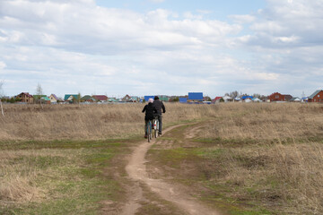 Two cyclists ride a road through a field